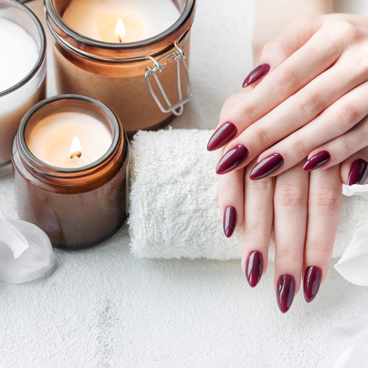 Beautiful hands of a young woman with dark red manicure on nails. Female hands on a towel in a nail salon, candles and white orchids flowers